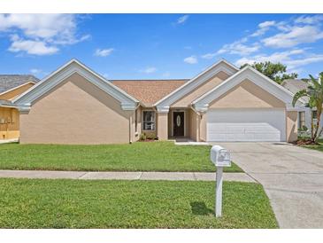 Tan house with a two-car garage, and nicely landscaped lawn at 9506 Pebble Glen Ave, Tampa, FL 33647
