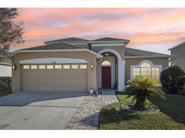 Tan house with red door, two car garage, and landscaped yard at 7720 Rathdown Ln, Wesley Chapel, FL 33545