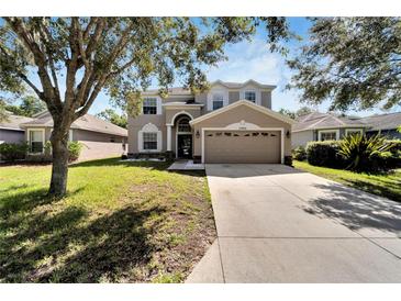 Two-story house with tan siding, large driveway, and landscaped yard at 13951 Caden Glen Dr, Hudson, FL 34669