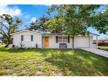 Newly renovated single story home with a bright orange front door and landscaped lawn at 5004 Flora Ave, Holiday, FL 34690