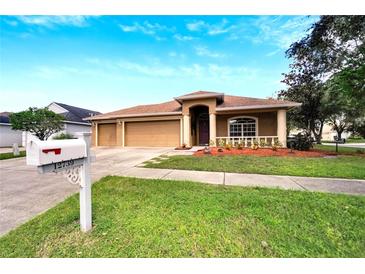 Tan three-car garage home with a red door and nicely landscaped yard at 12739 Standbridge Dr, Riverview, FL 33579