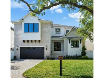 Beautiful two-story home with a manicured lawn, a brick driveway, and a black garage door underneath blue sky at 5024 W Dickens Ave, Tampa, FL 33629