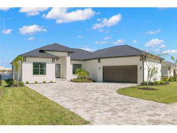 White one-story home with dark gray metal roof, paver driveway & landscaping at 1810 4Th E St, Palmetto, FL 34221