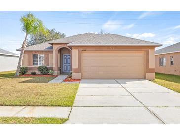 Tan house with blue door, two-car garage, and well-manicured lawn at 6340 Sushi Ct, Wesley Chapel, FL 33545