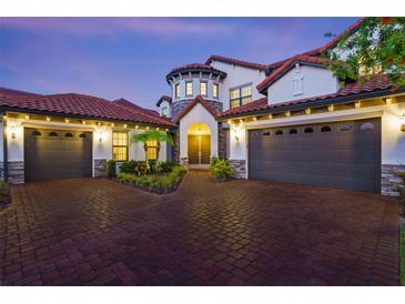 Elegant home featuring a brick driveway, three-car garage, stone accents, and a barrel tile roof at dusk at 8414 Dunham Station Dr, Tampa, FL 33647