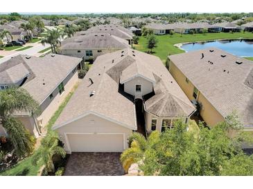 An aerial view of a beige single Gathering home with a lake and manicured lawns in a residential community at 1804 Pacific Dunes Dr, Sun City Center, FL 33573