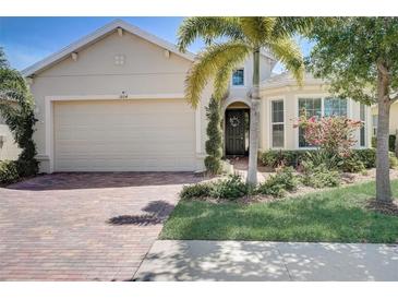 Tan house with brick driveway, palm trees, and manicured landscaping at 1804 Pacific Dunes Dr, Sun City Center, FL 33573