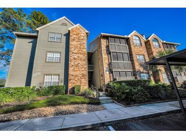 Exterior view of a two-story condo building with brick and siding exterior, screened balconies, and lush landscaping at 2500 Winding Creek Blvd # E102, Clearwater, FL 33761