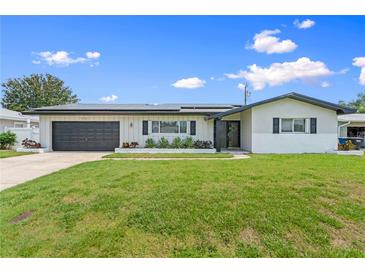 Charming one-story home with a well-manicured lawn, a dark garage door, and beautiful landscaping at 2132 Academy Dr, Clearwater, FL 33764