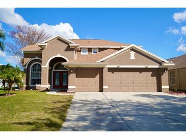 Two-story house with tan exterior, three-car garage, and manicured lawn at 2012 Fern Ridge Ct, Holiday, FL 34691