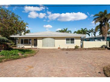 Bright yellow single-story home with brick driveway, palm trees, and a glass-block accent wall at 10244 Tarpon Dr, Treasure Island, FL 33706