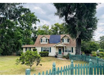 House exterior with solar panels, green fence, and mature trees at 14303 14Th St, Dade City, FL 33523