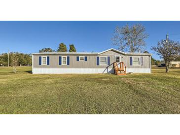 Gray manufactured home with blue shutters, situated on a spacious grassy lot at 40251 Laird Ave, Zephyrhills, FL 33540