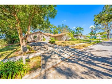 Tan house with a large yard and driveway, surrounded by lush green trees at 695 Sandy Hook Rd, Palm Harbor, FL 34683