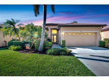 Tan one-story home with a two-car garage, lush landscaping, and palm trees at 5806 Hidden Falls Ln, Apollo Beach, FL 33572