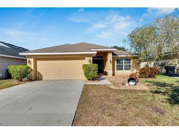 Single-story house with a beige exterior, two-car garage, and landscaped yard at 10739 Standing Stone Dr, Wimauma, FL 33598