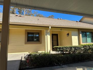 Exterior view of condo, featuring a light yellow building with a covered carport and landscaping at 2505 Oakleaf Ln # 24C, Clearwater, FL 33763