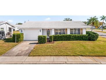 Charming single-story home featuring a well-manicured front yard with lush green hedges and a white tile roof at 9201 40Th N Way, Pinellas Park, FL 33782