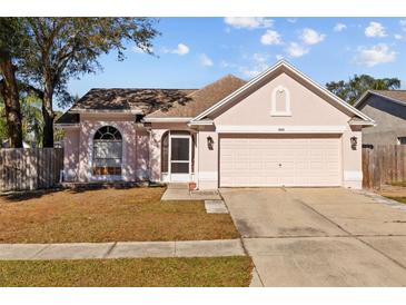 One-story house with pink stucco exterior, two-car garage, and fenced yard at 1202 Sawdust Ct, Valrico, FL 33596
