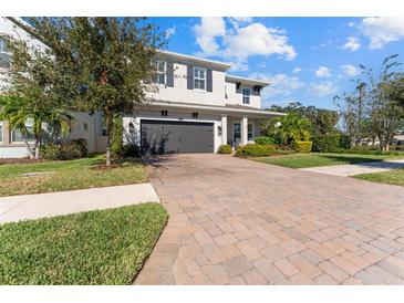 Two-story home with gray siding, dark garage door, and a brick paver driveway at 12107 Rustic River Way, Tampa, FL 33635