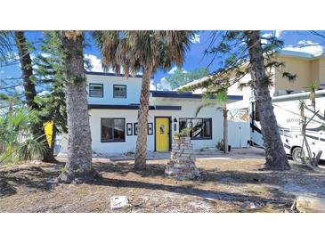 Cute two-story home with a yellow door, surrounded by palm trees at 14016 Marguerite Dr, Madeira Beach, FL 33708