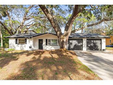 Updated Ranch home features a white brick exterior, black garage doors, and mature landscaping at 1408 Riverside Dr, Tarpon Springs, FL 34689