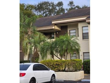 Exterior view of condo building with lush landscaping and a white car parked in front at 3540 Countrybrook Ln # D22, Palm Harbor, FL 34684