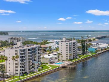 Aerial view of waterfront condominium buildings with a pool, boat dock, and nearby bridge at 300 Woodette Dr # 303D, Dunedin, FL 34698