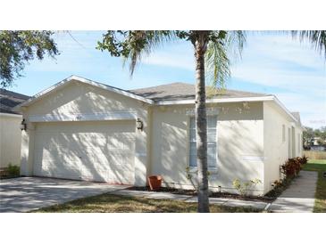 Beige single-story home featuring an attached two-car garage, neutral landscaping, and a sidewalk at 7833 Carriage Pointe Dr, Gibsonton, FL 33534