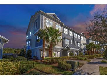 Three-story townhome at sunset; gray siding, white garage doors, landscaping at 4069 Rocky Shores Dr, Tampa, FL 33634