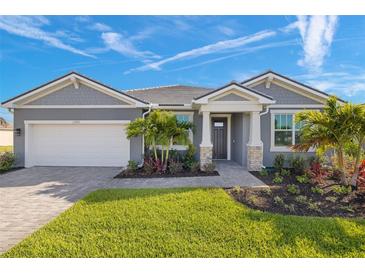 Beautiful gray house with stone accents, manicured lawn and garden, and a brick driveway on a sunny day at 11971 Starbright Path, Venice, FL 34293