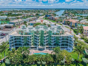 Aerial view of a green multi-story building with pool and lush landscaping, near the water at 11605 Gulf Blvd # 502, Treasure Island, FL 33706