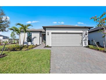 Charming single-story home featuring a gray two-car garage, paver driveway, manicured lawn, and tropical landscaping at 3065 Winding Creek Trl, North Port, FL 34289