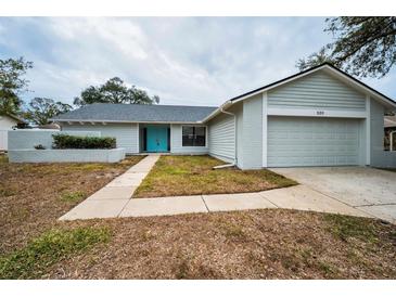 Charming single-story home with teal front door, attached garage, and landscaping at 520 Meravan Dr, Palm Harbor, FL 34683