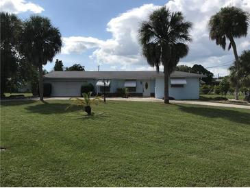 Light blue, single-story home with a two-car garage, surrounded by palm trees and a green lawn at 644 Blue Nw Ln, Port Charlotte, FL 33952
