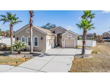 Tan house with palm trees, two-car garage, and a paved driveway at 12865 Ione Way, Spring Hill, FL 34609