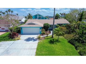 Charming single-Gathering home features lush landscaping, bright turquoise exterior, and a two-car garage at 2993 W Vina Del Mar Blvd, St Pete Beach, FL 33706