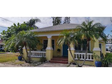 Charming yellow home with a front porch, white railings, and lush landscaping at 301 Hope St, Tarpon Springs, FL 34689