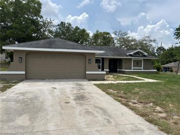 Tan single-story home featuring a two-car garage, green lawn, and a neutral color scheme at 12186 Lamont Dr, Spring Hill, FL 34608