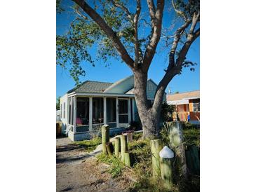 Quaint light blue home with screened-in front porch and large tree at 13318 2Nd E St, Madeira Beach, FL 33708