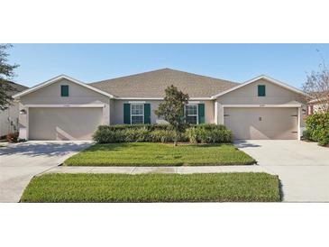 Tan two-unit house with green accents, two-car garages, and well-manicured lawn at 10347 Heron Hideaway Loop, Land O Lakes, FL 34638