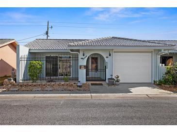 Light blue house with a white garage door, black gate, and landscaped yard at 10449 Larchmont N Pl, Pinellas Park, FL 33782