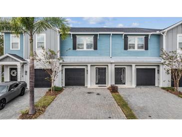 Three-unit townhome building with light blue siding, black garage doors, and a paved driveway at 2919 Grand Kemerton Pl, Tampa, FL 33618