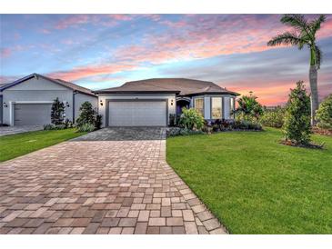 Single story home with a two-car garage and manicured lawn at sunset at 8705 Coastal Key Way, Parrish, FL 34219