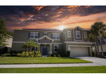 Two-story house with a green exterior, three-car garage, and landscaping at 26888 Fiddlewood Loop, Wesley Chapel, FL 33544