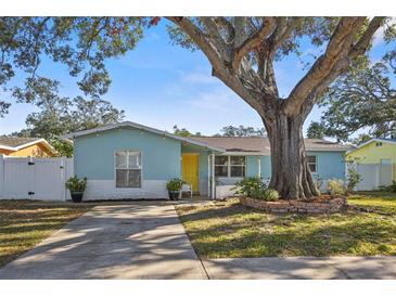 Charming light blue house with a yellow door, landscaping, and large tree at 2209 Gladys St, Largo, FL 33774