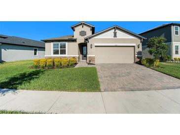 One-story house with tan siding, stone accents, and a two-car garage at 7122 Heron Walk Ln, Wesley Chapel, FL 33545