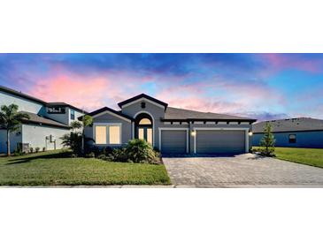 Charming one-story home featuring a two-car garage, paver driveway, well-maintained lawn, and colorful sunset sky at 9152 Warm Springs Cir, Parrish, FL 34219