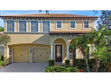 Two-story home showcasing a tile roof, tan stucco, arched entry, manicured landscaping, and a two-car garage at 20314 Chestnut Grove Dr, Tampa, FL 33647