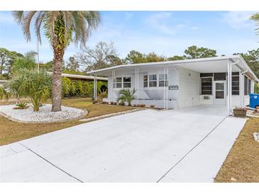 Charming single-story home with a pristine white exterior, spacious carport and manicured landscaping with palm trees at 14912 Brookridge Blvd, Brooksville, FL 34613
